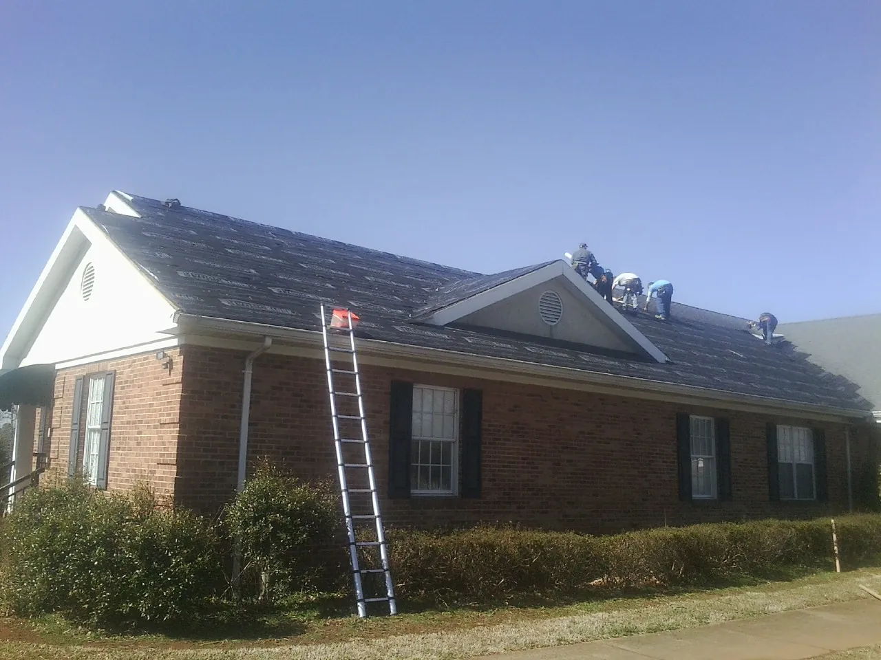 Crew tearing shingles off a brick ranch roof with a ladder set — Emergency Roof Repair work by our crew in Horton