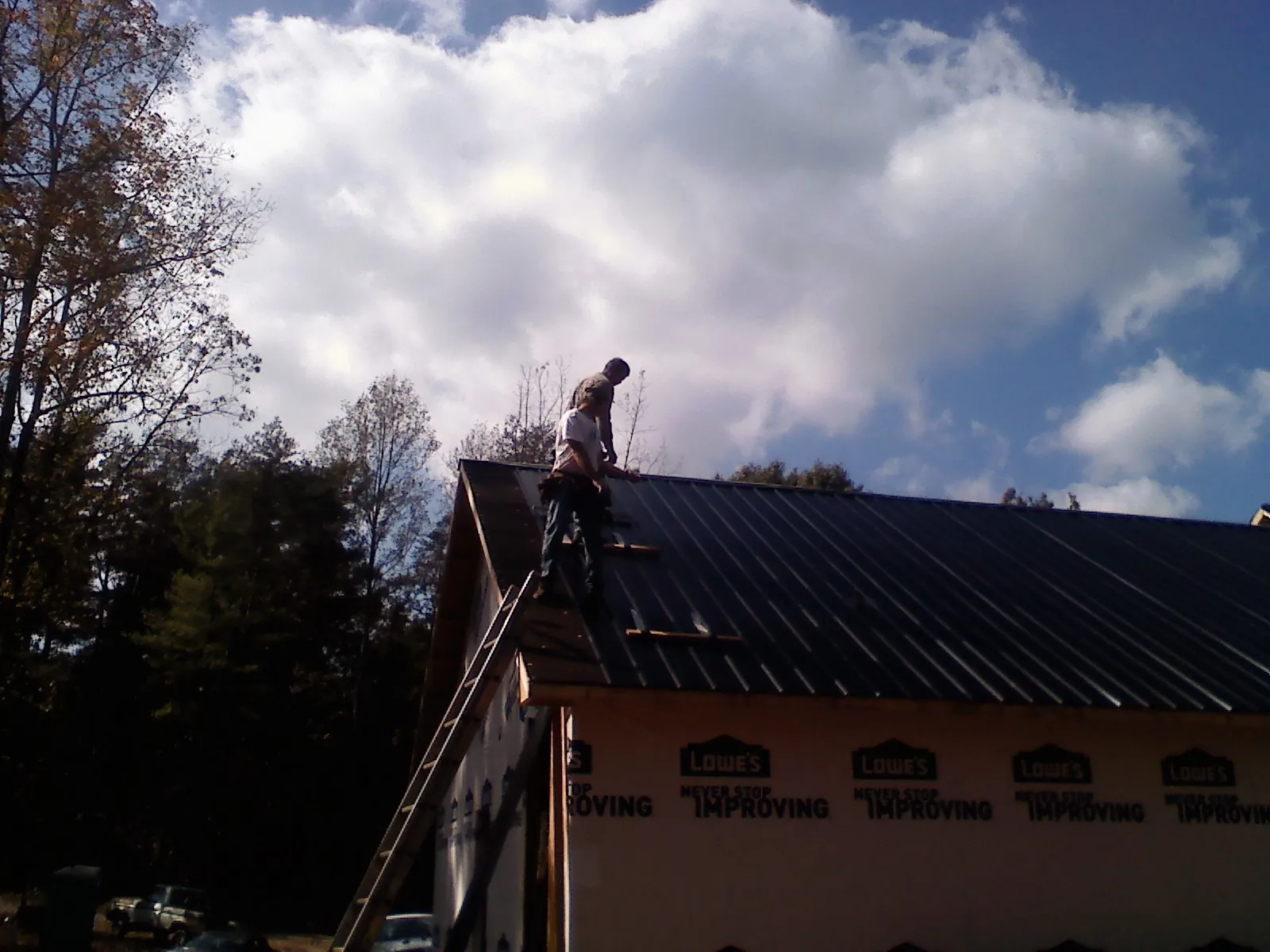 Roofer fastening dark metal panels high against a cloudy sky, from a Roof Inspection job in Horton